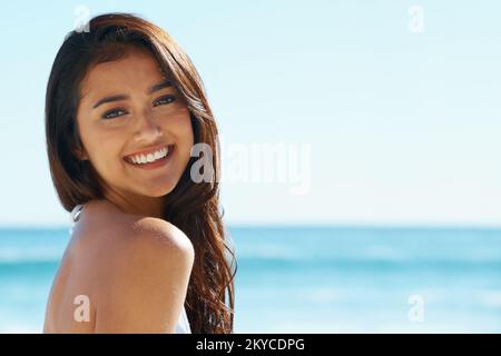 Catching a tan and feeling great. A gorgeous young woman standing on the beach in the sunshine. Stock Photo