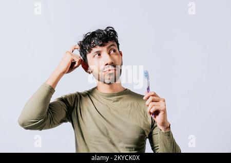 Thoughtful man holding toothbrush isolated, Portrait of young man thinking holding toothbrush. Man holding toothbrush with pensive expression Stock Photo