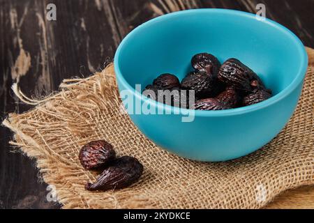 Dried mission figs in glass bowl on burlap and wooden background. Stock Photo
