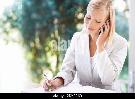 Staying on top of her schedule. An attractive young businesswoman taking notes while speaking on her cellphone. Stock Photo