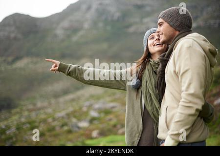 This view is stunning. A young couple admiring the view while out hiking during winter. Stock Photo
