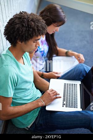Using research resources. Two young students doing research on a laptop and in a textbook. Stock Photo