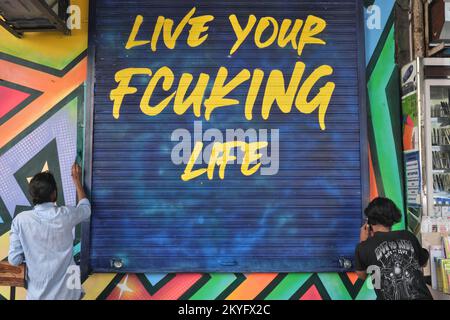 Workers in Mumbai, India, painting a shop entrance, including the slogan Live Your Fcukin Life on the door shutters Stock Photo