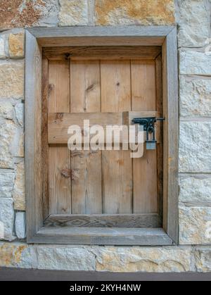 San Antonio, Texas- Wood window cover with padlock. Small window close-up with wood cover and frames in the middle of rough stone walls. Stock Photo