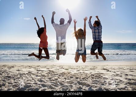 Celebrating summer time. Rear view of two young couple jumping together on the beach. Stock Photo