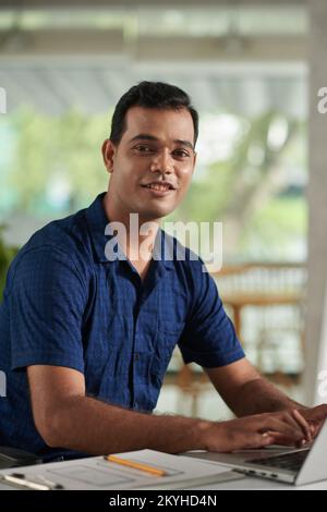 Portrait of smiling lead UX designer working on laptop at office desk Stock Photo
