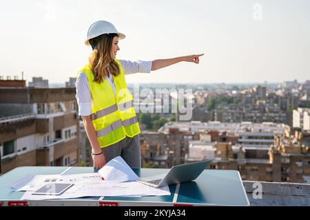 Young female construction specialist engineer reviewing blueprints at construction site Stock Photo