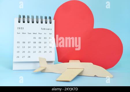 Selective focus of February 2023 desk calendar on blue background with wooden airplane model and big red heart shape. Travel and holiday vacation Stock Photo