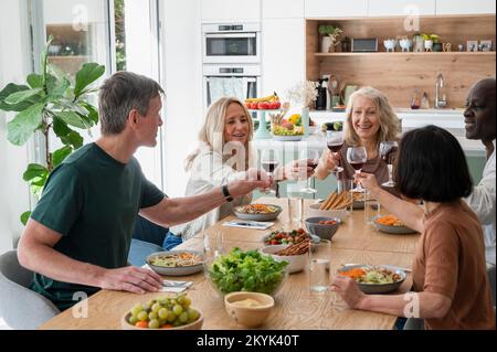 Diverse group of senior friends making a toast while enjoying a meal together at home Stock Photo