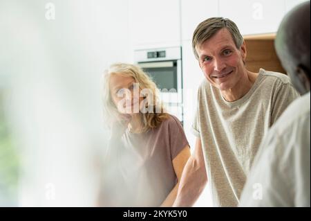 Portrait of middle-aged couple chatting with friends in kitchen Stock Photo