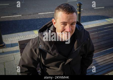 Man sitting on a bench in Liverpool and smiling in to camera Stock Photo