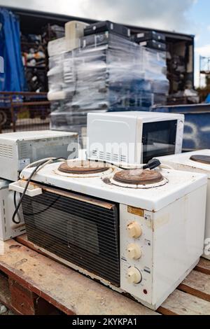 Old broken small hot plate oven and other old e-waste appliances pilled up in the background. Stock Photo