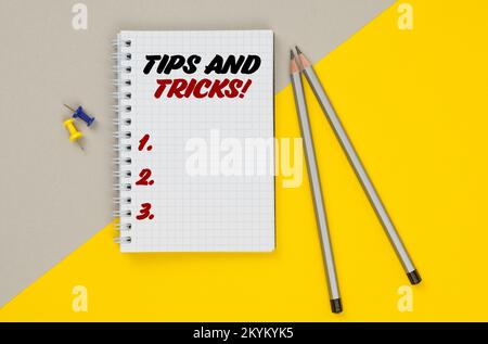 Business and finance. On a yellow-gray background are pencils, buttons and a notebook in which it is written - Tips And Tricks Stock Photo