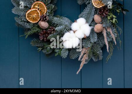 Part of Christmas wreath with pine branches, pine cones, nuts on blue door background with space for text Stock Photo