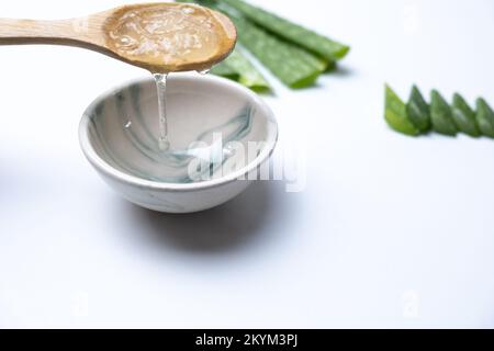 Aloe vera slices on white background, aloe vera gel pouring from wooden spoon. Stock Photo