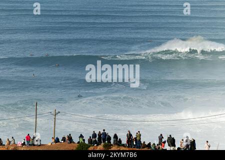 People watching the big giant waves crashing in Nazare, Portugal. Biggest waves in the world. Touristic destination for surfing. Stock Photo