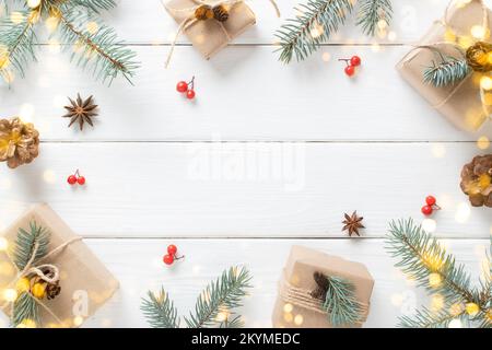 Christmas background with eco-packed gifts, blue fir branches and festive bokeh on a white wooden background. Copy space. Flat lay, top view. Stock Photo