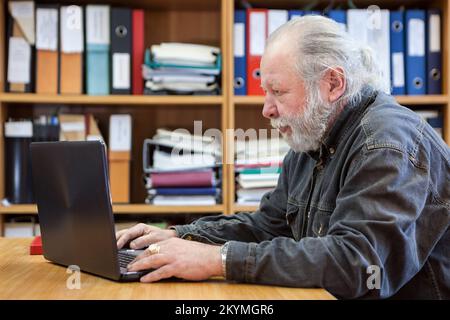 Elderly man with laptop at workplace in office, side view Stock Photo