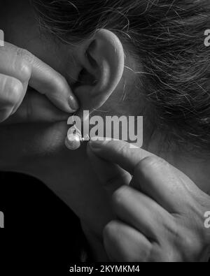 Close-up view of a woman putting on a pearl earring, in black and white Stock Photo
