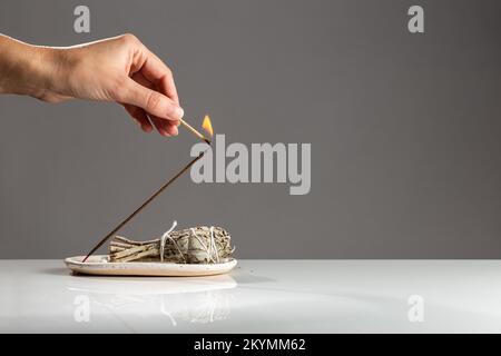 Female Hand Kindle Aromatic Incense Smudge Stick with a Match for Meditation and Relax on Dark Minimalistic Background. Aromatherapy Smoke is Used to Stock Photo
