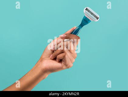 Crop hand of black woman demonstrating modern disposable convenient razor on turquoise background Stock Photo
