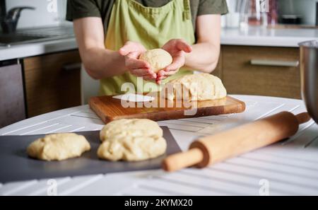 Male chef baker in green apron making dough balls with wooden cutting board on background. Working at home kitchen concept, homemade baking. High quality image Stock Photo