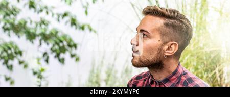 Horizontal banner or header with young pensive hipster man looking up outdoor at the garden - Focus on face Stock Photo