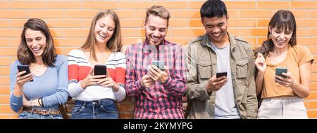 Horizontal banner with multicultural friends having fun together looking at their smartphones  at wall on college campus - Young people addicted by mo Stock Photo