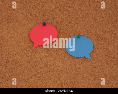 A blank red speech bubble and a blank blue speech bubble pinned to a corkboard. Close up. Stock Photo