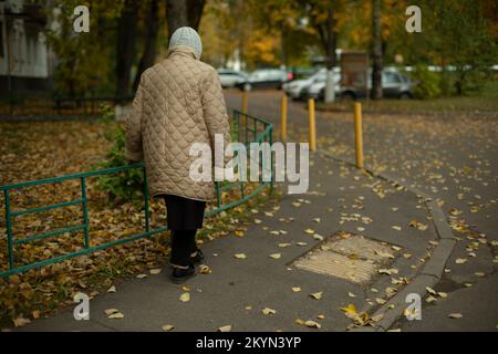 Pensioner walks down street in autumn. Old woman walks in city. Old woman walks path. Stock Photo