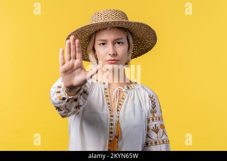 Uninterested ukrainian woman disapproving with NO hand sign gesture. Denying, rejecting, disagree. Portrait of young lady on yellow background Stock Photo