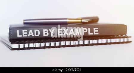 Business and education concept. On the table are a notebook, a pen and a book. The book says - LEAD BY EXAMPLE Stock Photo