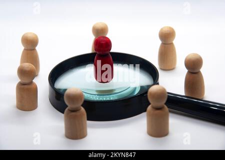 Red wooden doll on top of magnifying glass surrounded with other wooden figure. Stock Photo