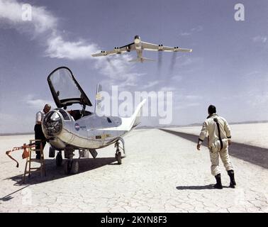 NASA research pilot Bill Dana takes a moment to watch NASA's NB-52B cruise overhead after a research flight in the HL-10. On the left, John Reeves can be seen at the cockpit of the lifting body. The HL-10 was one of five lifting body designs flown at NASA's Dryden Flight Research Center, Edwards, California, from July 1966 to November 1975 to study and validate the concept of safely maneuvering and landing a low lift-over-drag vehicle designed for reentry from space. Northrop Corporation built the HL-10 and M2-F2, the first two of the fleet of 'heavy' lifting bodies flown by NASA. The contract Stock Photo