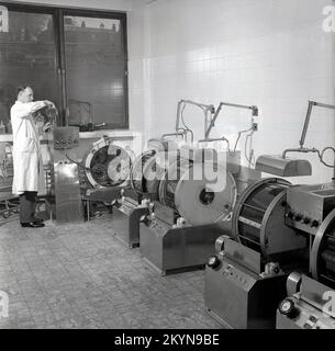 1950s, historical, inside a room at a factory, a male research scientist with glass bottles mixing liquids, chemicals that produce colours for dying clothing and other textiles, England, UK. Equipment of the era can be seen in the picture, which are used for testing colour dyes. Stock Photo