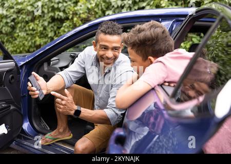 Excited father showing mobile phone to son leaning on car door Stock Photo