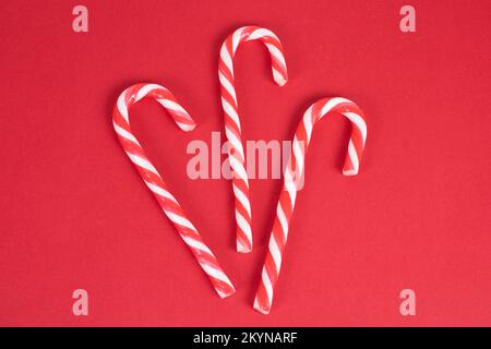 Three red and white candy canes on red christmas background, top view, mock up and template for postcards, banners Stock Photo