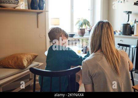 Rear view of mother helping son with homework at home Stock Photo