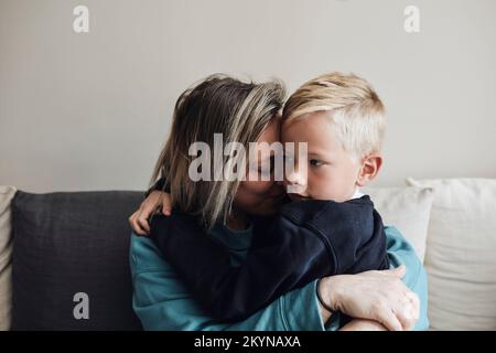 Mother embracing son while sitting on sofa at home Stock Photo