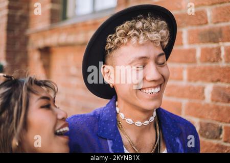 Happy young man wearing hat by female friend laughing against building Stock Photo