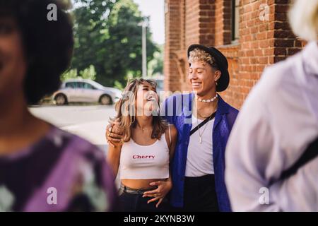 Happy young man wearing hat while walking with arm around woman Stock Photo