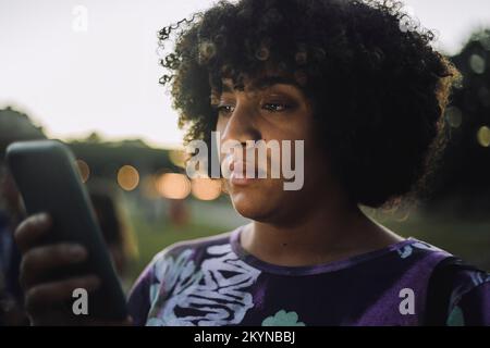 Transgender woman with curly hair using smart phone during sunset Stock Photo