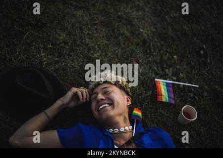 Happy young men with eyes closed lying by rainbow flag on grass Stock Photo