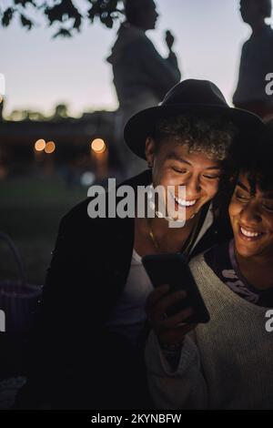 Happy transgender woman sharing mobile phone with male friend during sunset Stock Photo