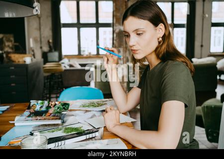 Thoughtful female food stylist puckering lips and holding pen while working in studio Stock Photo