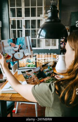 Young food stylist looking at photographs while working in studio Stock Photo