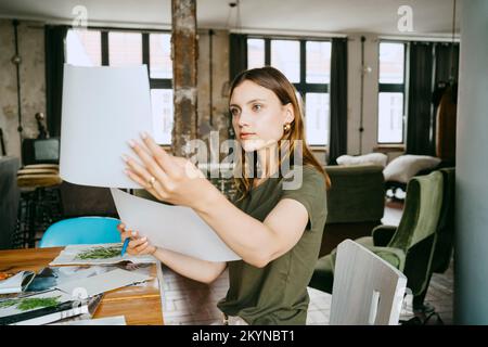 Young female entrepreneur comparing photographs at table in studio Stock Photo