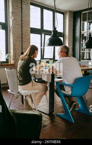 Male and female business colleagues discussing over laptop while sitting on chair in studio Stock Photo