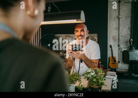 Happy male photographer holding digital camera while looking at colleague in studio Stock Photo