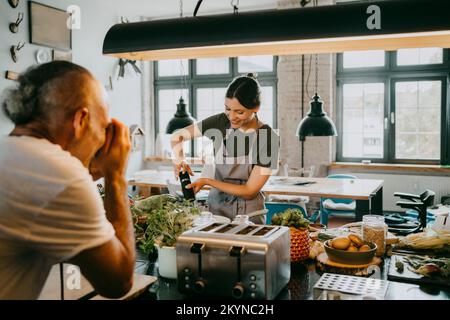 Smiling young female chef preparing food with photographer taking picture in studio kitchen Stock Photo